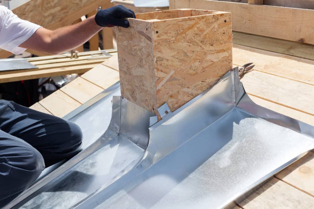 Zingueur installant un habillage de cheminée en OSB avec de la tôle sur une toiture en bois en plein jour.