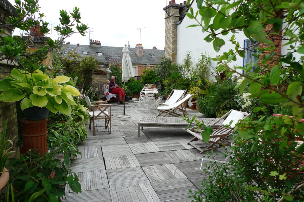 Terrasse de toit verdoyante avec sol en bois. Un homme et une enfant lisent sur un banc, entourés de plantes et mobilier d'extérieur.